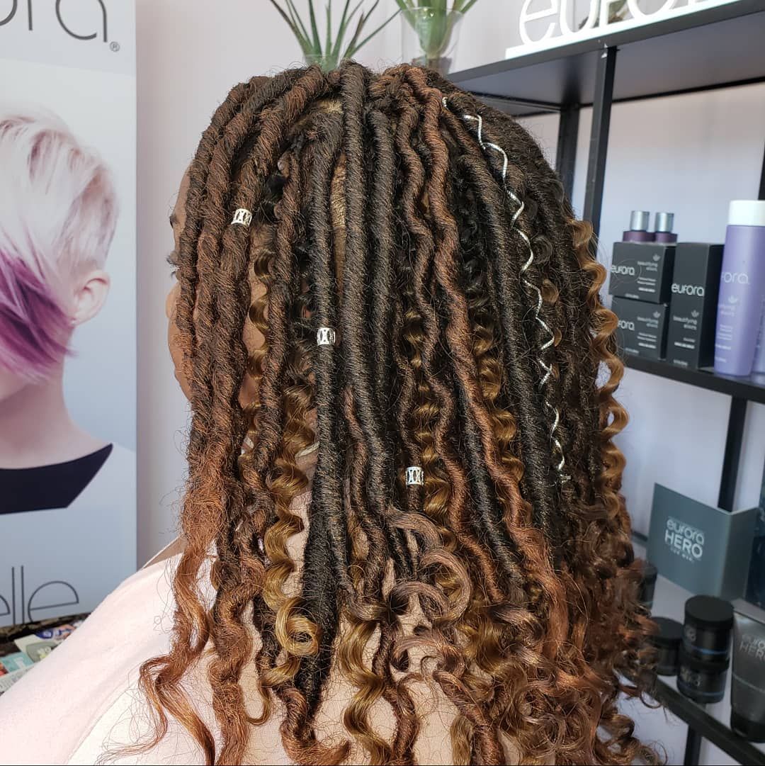 Back view of person with brown and copper locs, adorned with hair jewelry, in a salon.