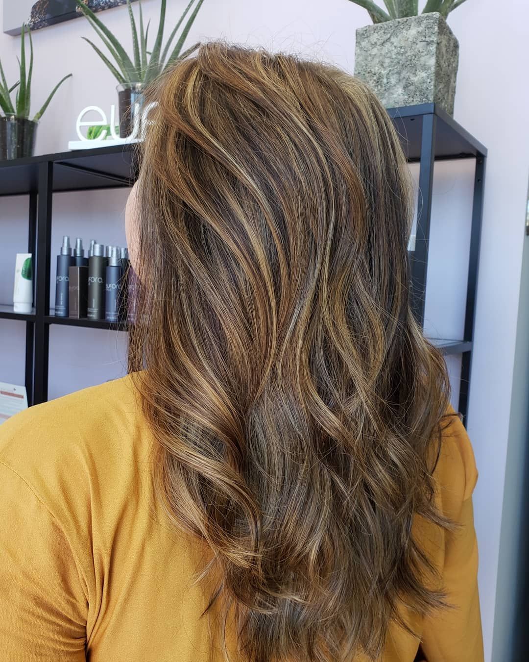 Woman's brown hair with blonde highlights, styled in loose waves, in a salon setting.