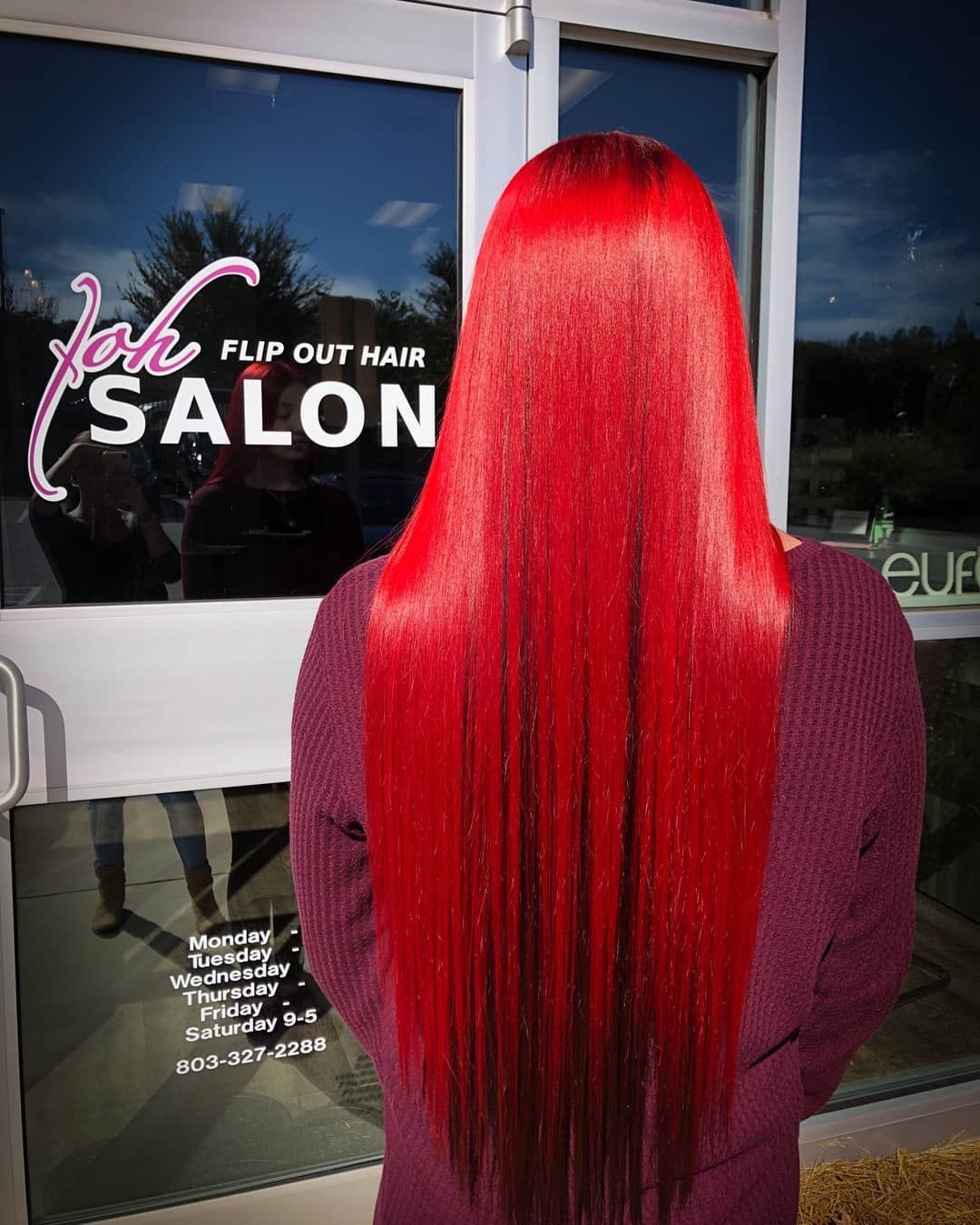 Person with long, straight, vibrant red hair stands in front of a salon door with a 