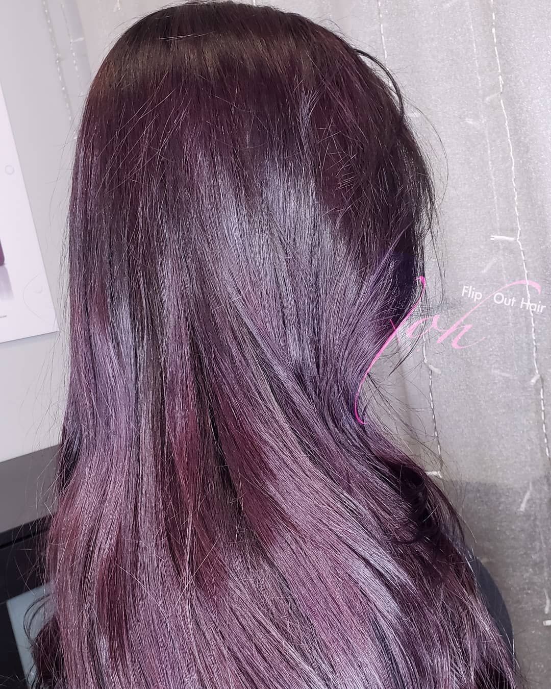 Woman with long, dark, purple-tinted hair, viewed from the side, possibly indoors.