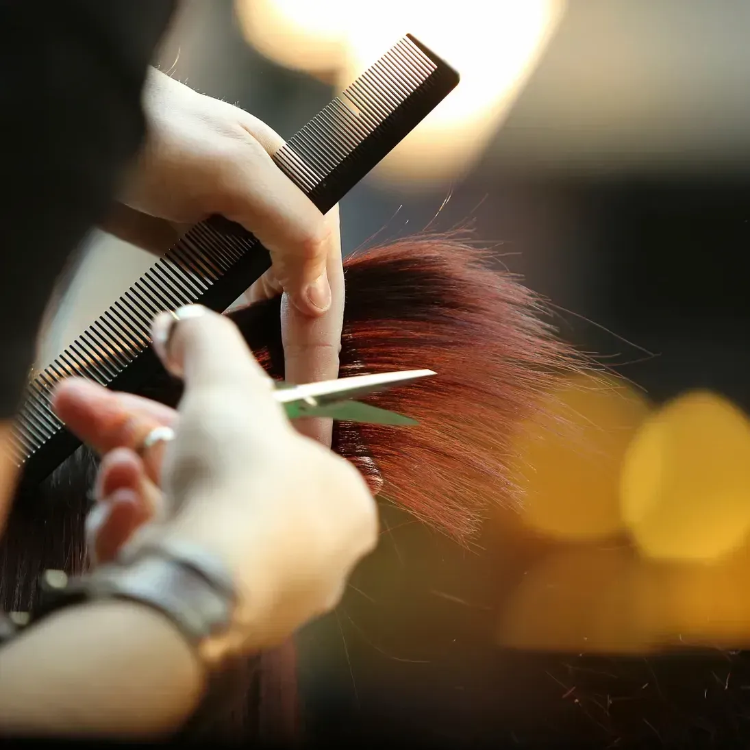 Hands cutting red hair with scissors and comb in a salon.
