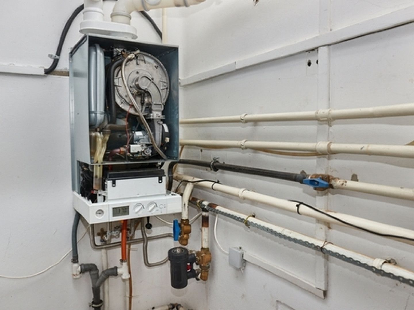 A wall-mounted gas boiler with exposed components and connected to pipes in a utility room.