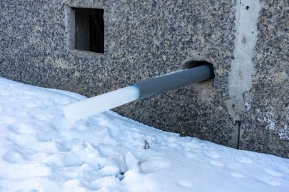 Gray pipe, partially ice-covered, exits a concrete wall. Snow covers the ground.