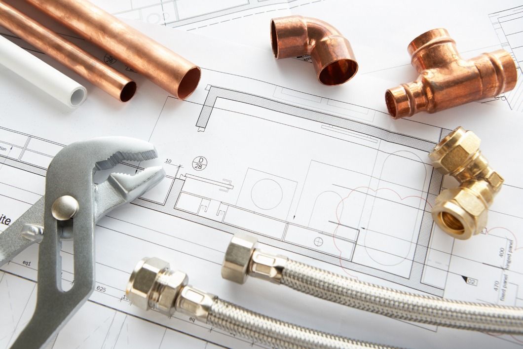 Plumbing tools and pipes on a blueprint: copper pipes, fittings, adjustable wrench, and flexible supply lines.