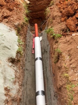 Trench with white conduit and orange wire, level in the trench, dirt and grass surrounding.