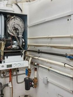 A gas boiler with pipes and valves against a white wall.