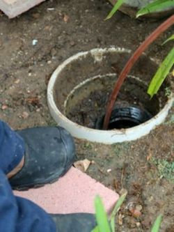 Person with boots uses a hose to flush a pipe in a dirty, outdoor well.