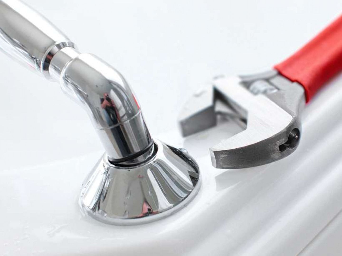 Wrench near a chrome faucet on a white surface; plumbing repair.