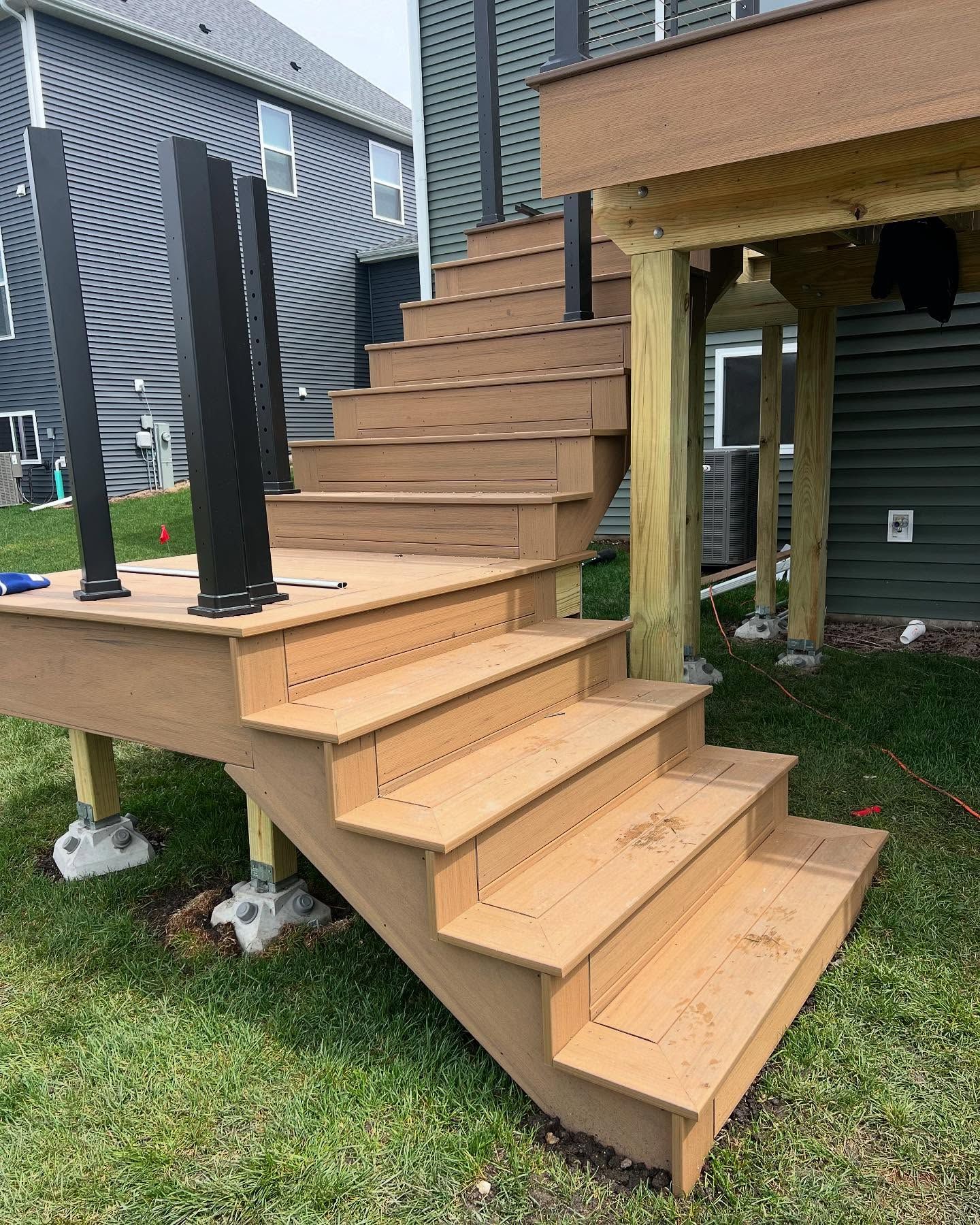 Wooden deck with stairs leading to a green grassy yard. Dark railing posts are visible on the deck.