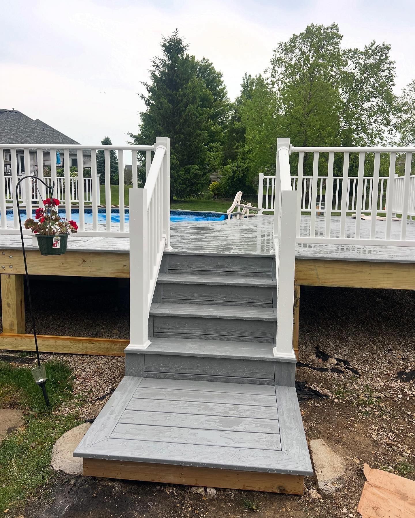 Grey wooden steps leading up to a deck with a white railing; a pool is visible in the background.
