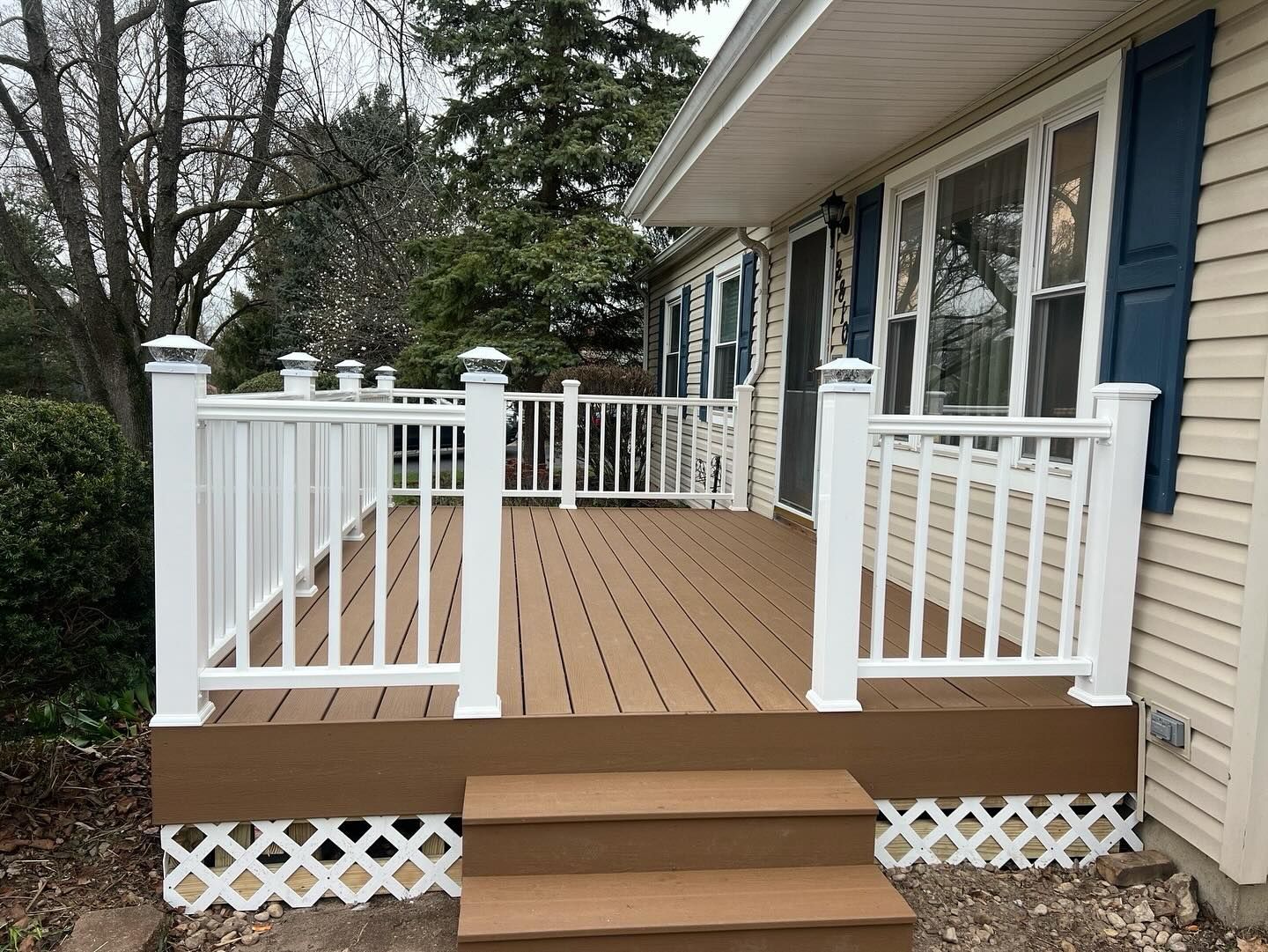 Brown composite deck with white railing, and stairs. The house is beige with blue shutters.