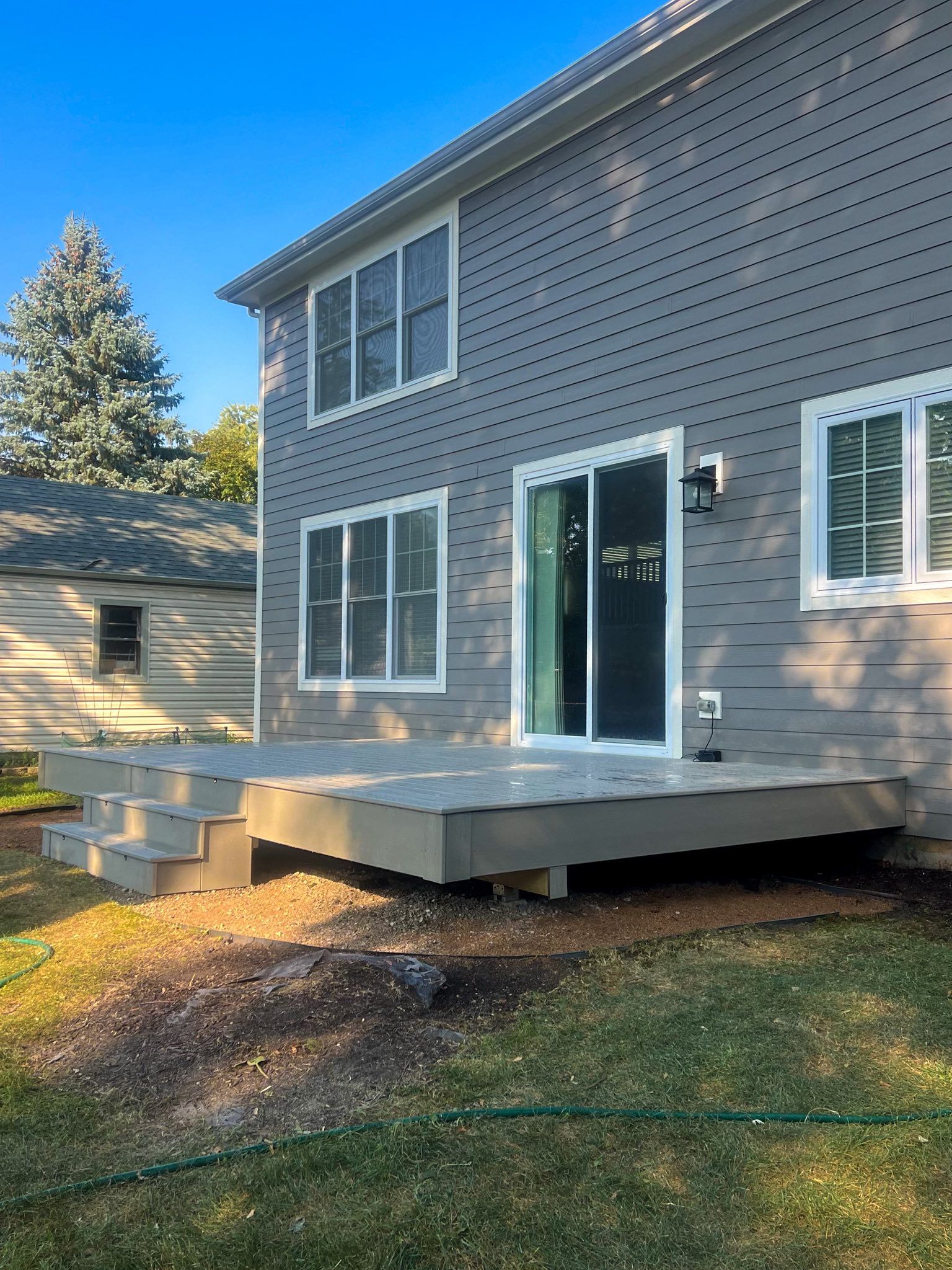 Gray two-story house with a matching deck and steps; a sliding door is visible.