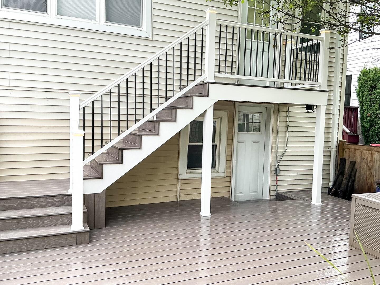 Deck with stairs and black railing against a light-colored building with a door underneath.