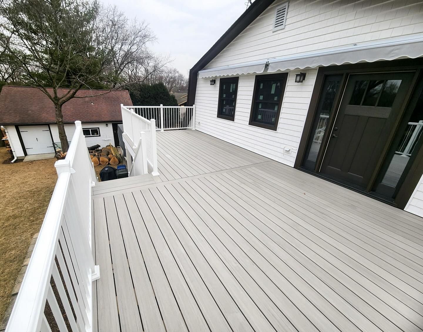 Elevated deck with white railing, light gray boards, and access to a white house with dark door and windows.