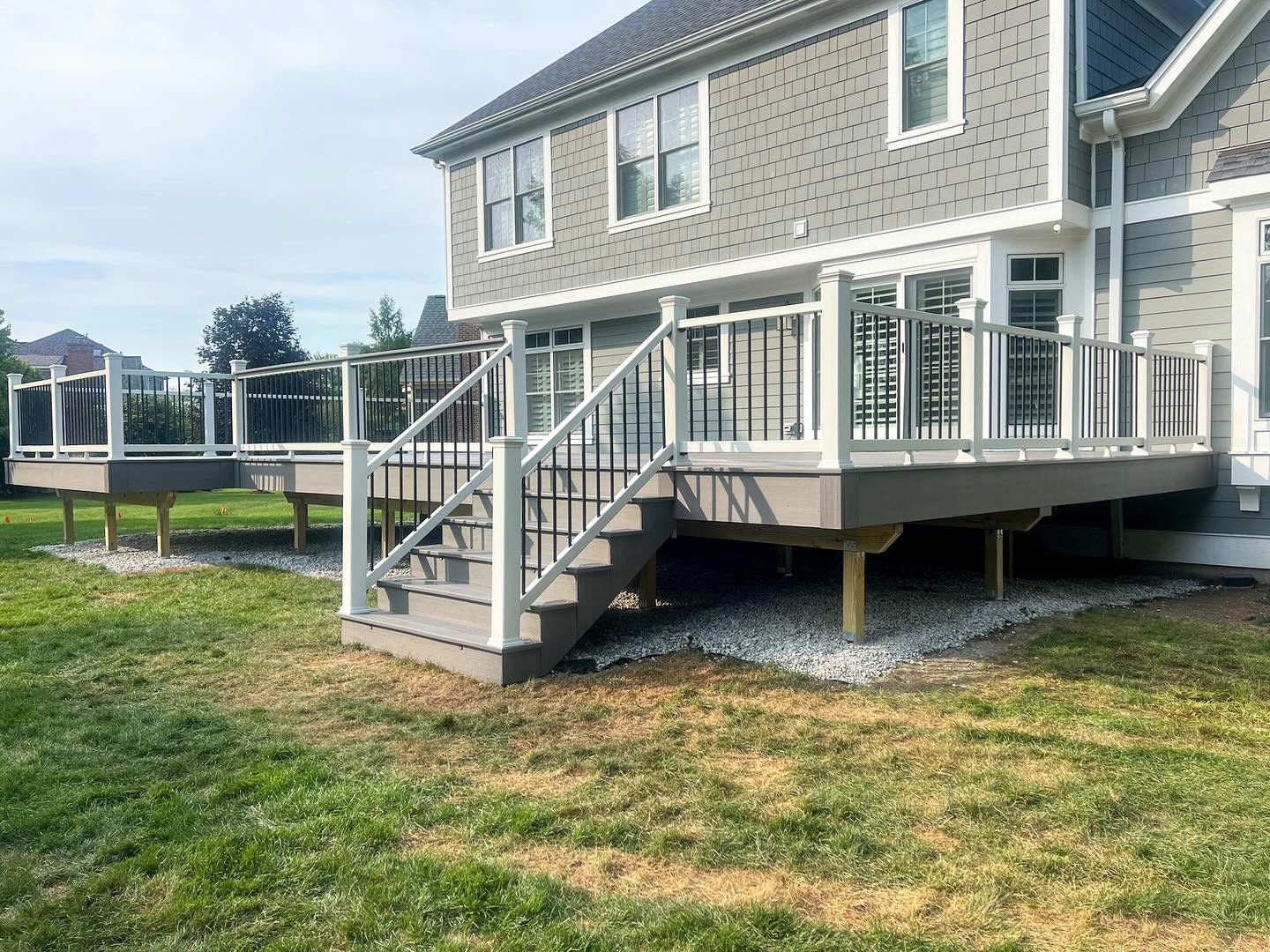 Gray deck with white railing and black spindles, attached to a gray house, on a grassy lawn.