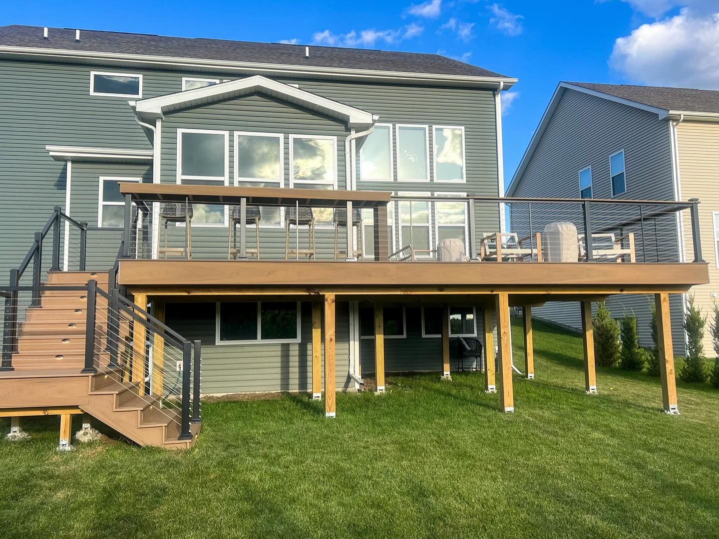 Backyard deck with brown composite boards, black railing, and green siding on a sunny day.