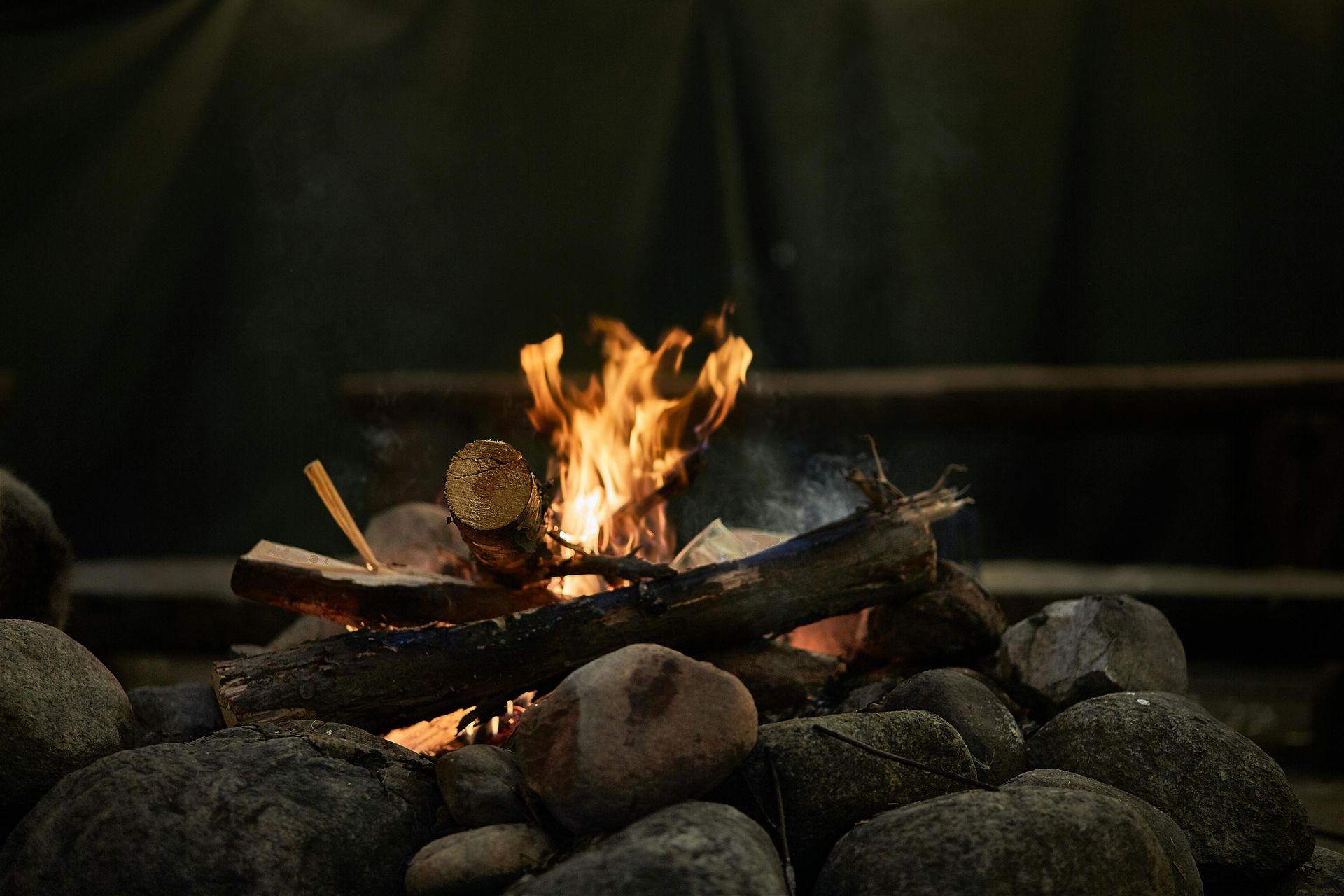 A campfire burns brightly, surrounded by rocks and logs, with a dark background.