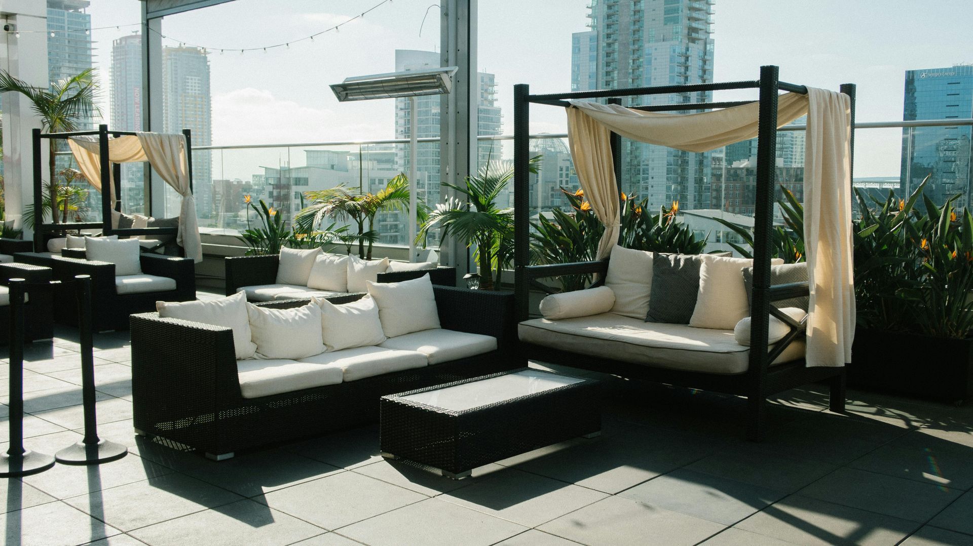 Rooftop lounge with white sofas, daybed, coffee table, and city skyline view.