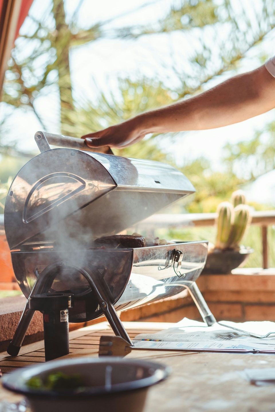Person grilling on a small outdoor barbecue. Steam rises from the grill.