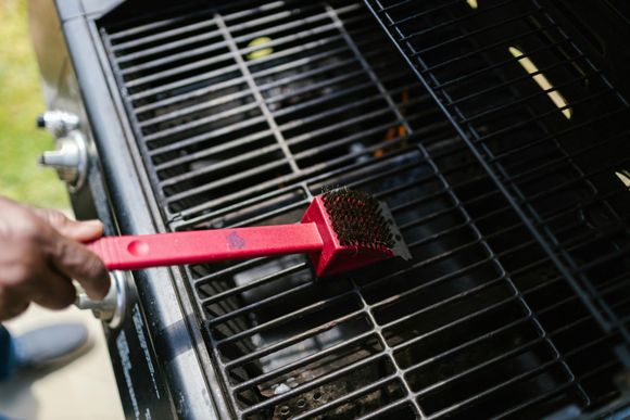 Person cleaning grill grates with a red brush on an outdoor grill.