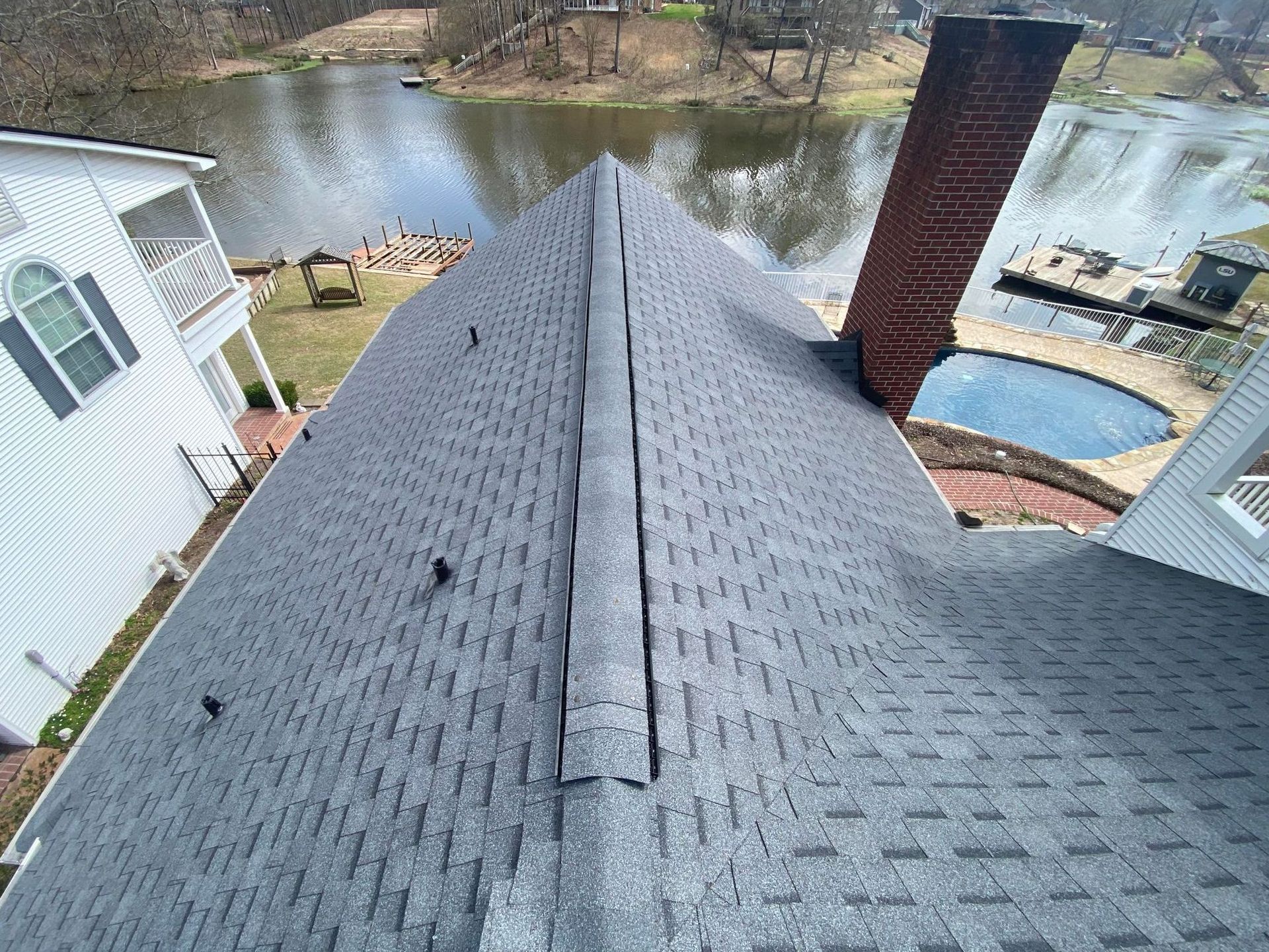 An aerial view of a roof with a chimney and a pond in the background.