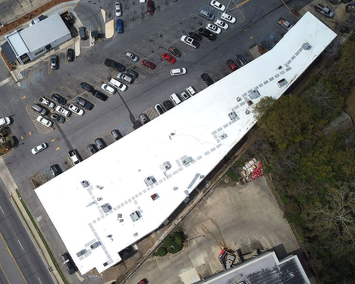 An aerial view of a building with a white roof and a parking lot.
