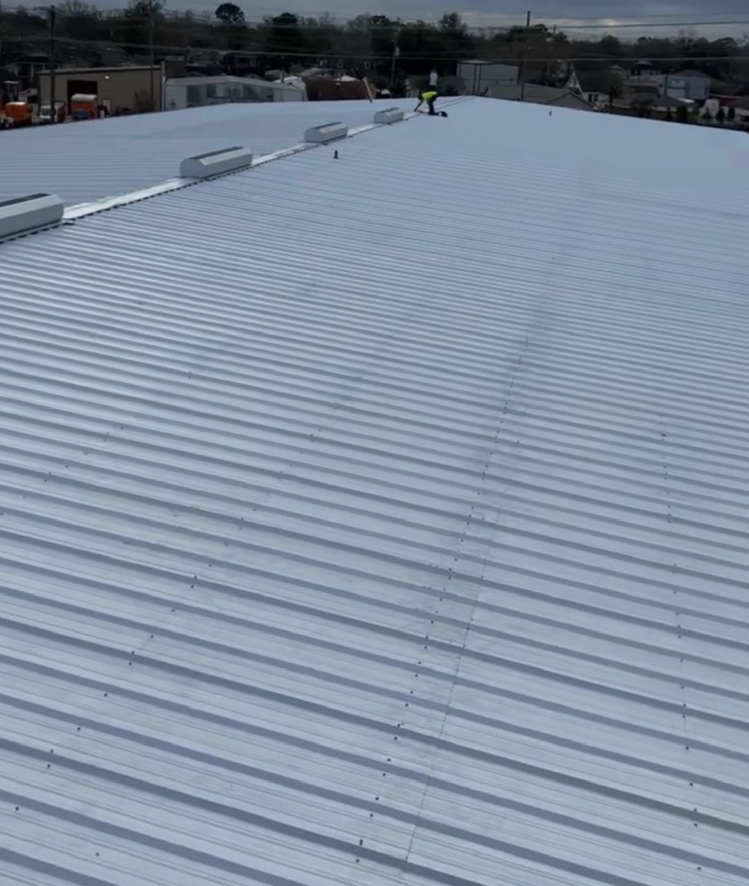 A man is standing on top of a white metal roof.
