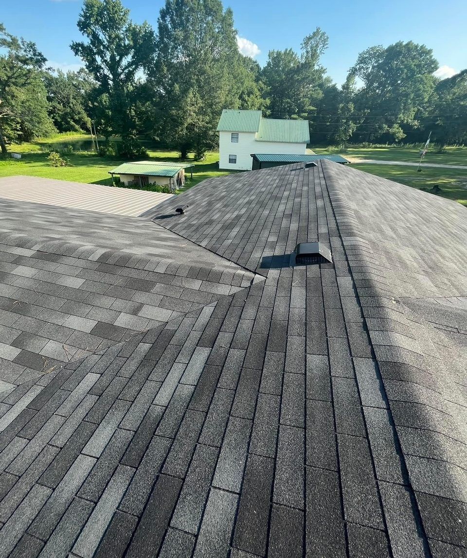 A roof with shingles on it and a house in the background.