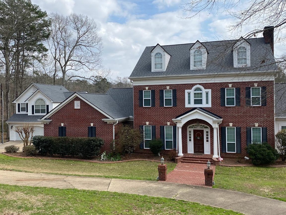 A large brick house with a gray roof and blue shutters is sitting on top of a lush green lawn.