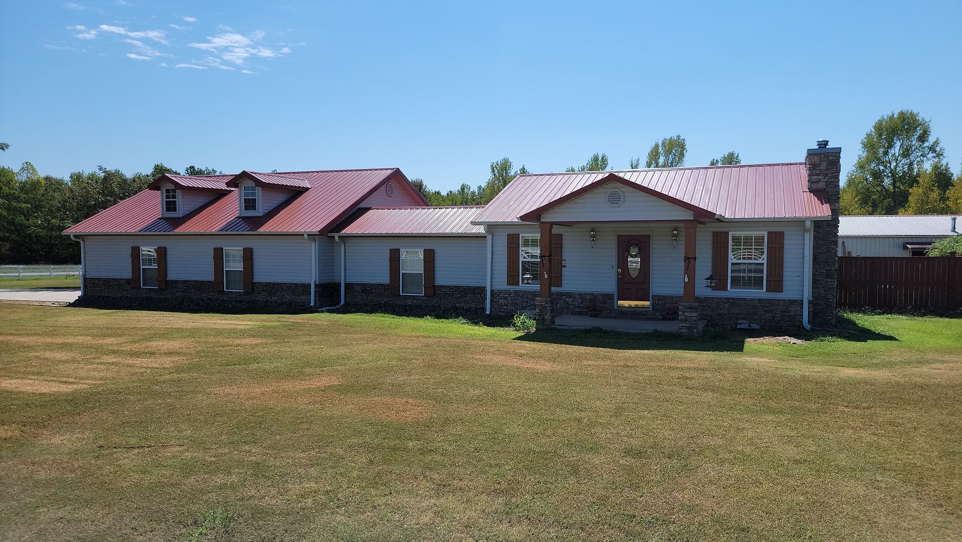 A large house with a red roof is sitting in the middle of a grassy field.