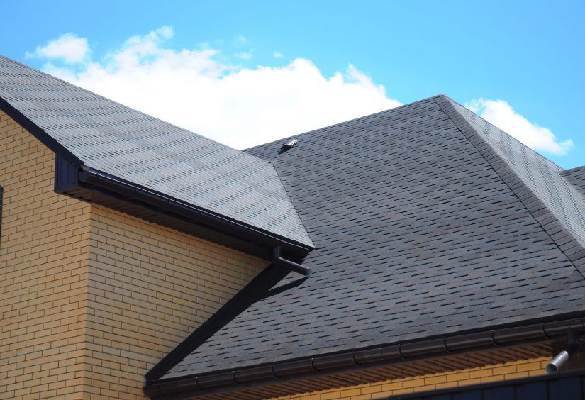 A brick house with a black roof and a blue sky in the background.