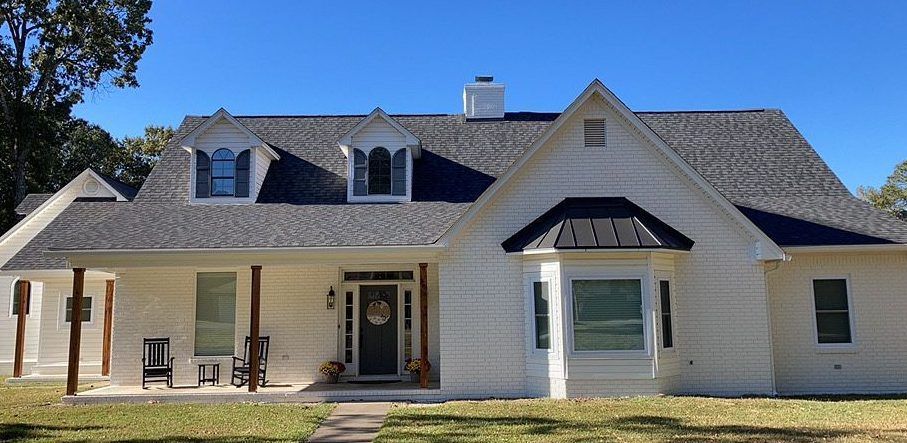 A large white house with a gray roof and a porch.