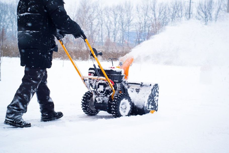 Person clearing snow with a snow blower on a snowy driveway