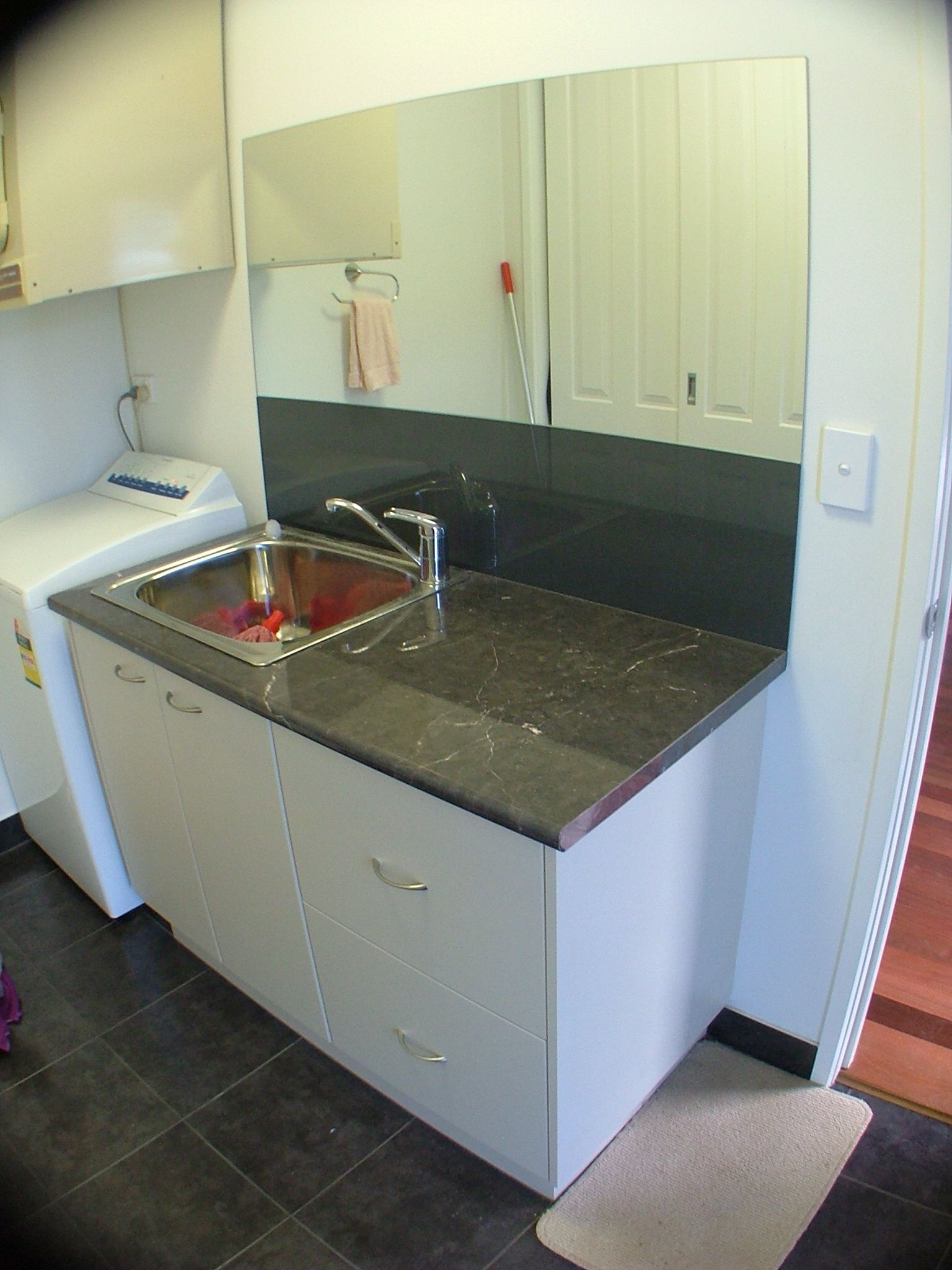 Laundry room with a sink, mirror, and countertop. A washing machine is visible to the left.