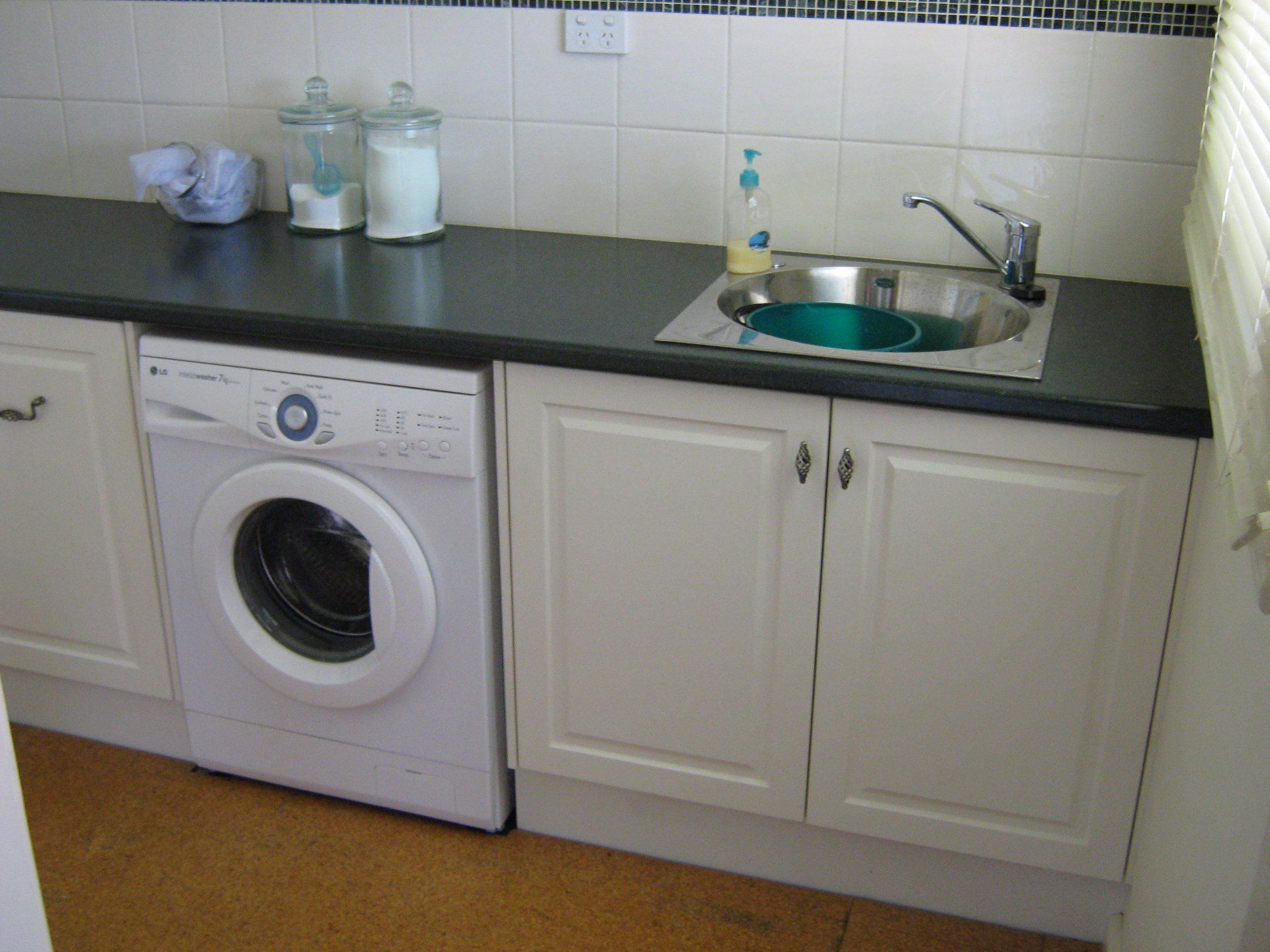 Laundry room with a washing machine, sink, and cabinets; light cabinets, dark counter.