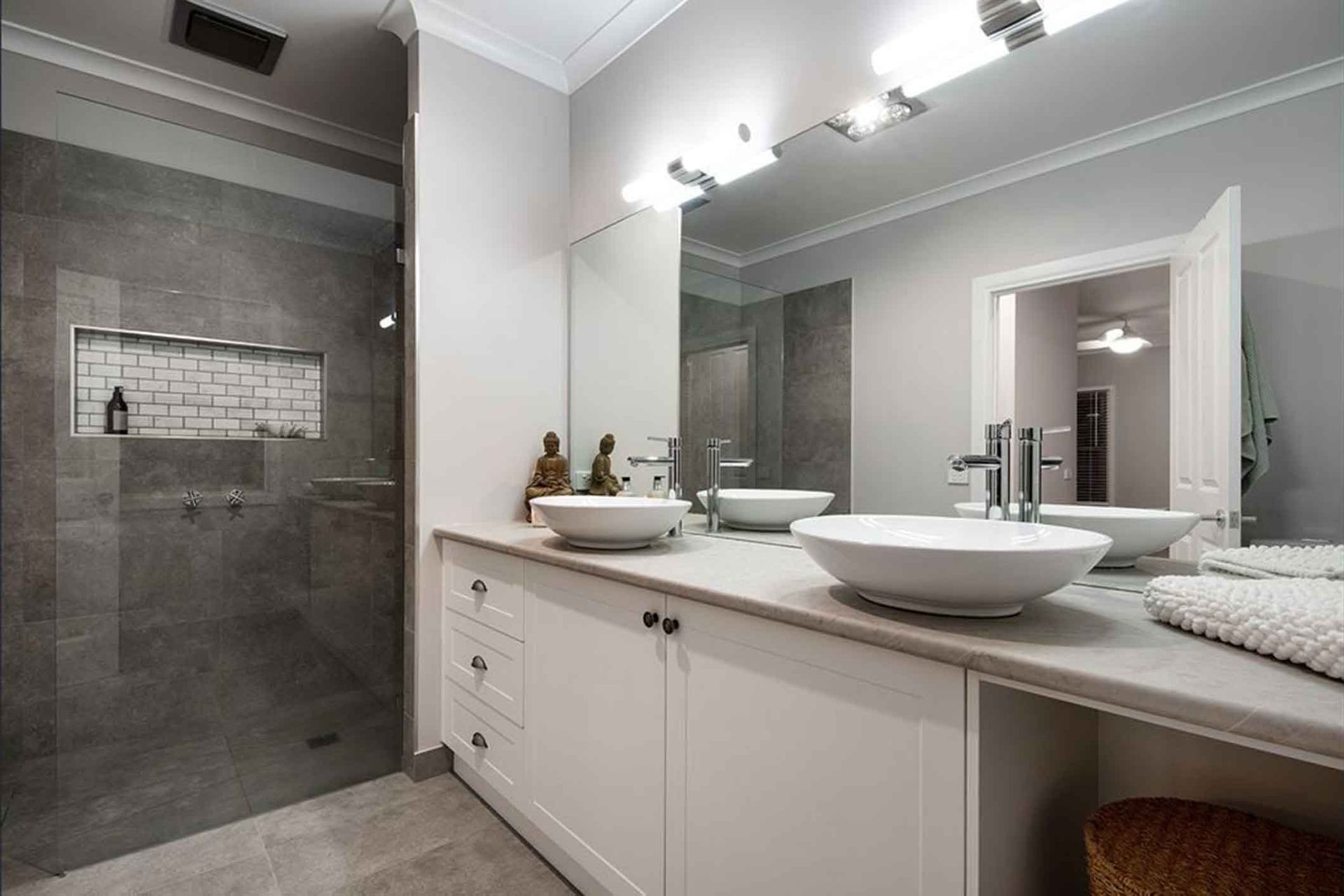 A modern bathroom with a gray tiled shower, double vanity with white sinks, and a light-filled doorway.