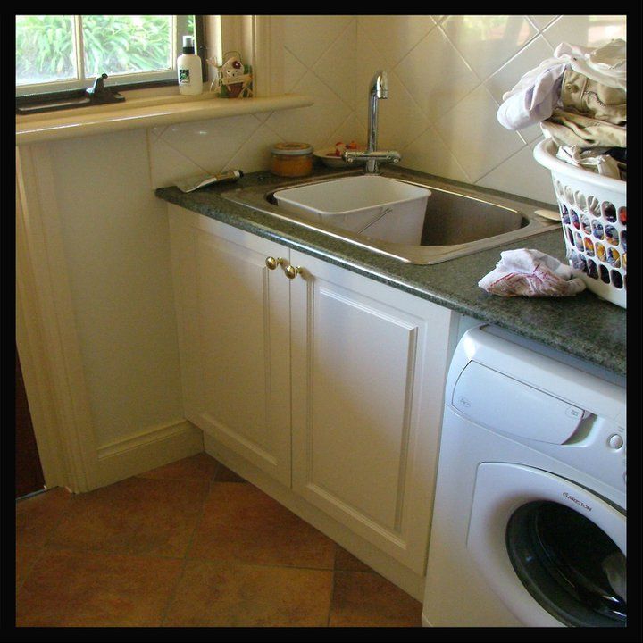 Laundry room with a white sink, cabinets, and washing machine. A full laundry basket sits beside the machine, and a small window is in the background.