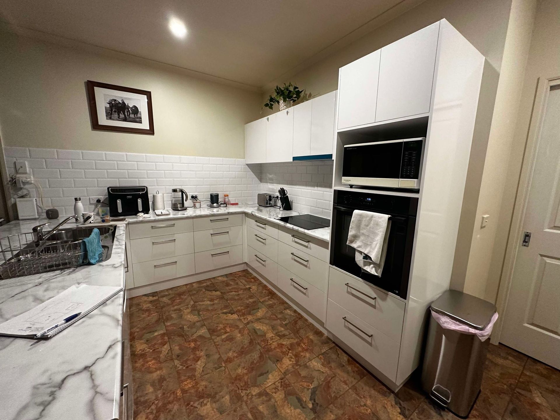 A white modern kitchen with stainless steel appliances, a microwave, oven, and cabinets. Marble countertops and a brick backsplash.