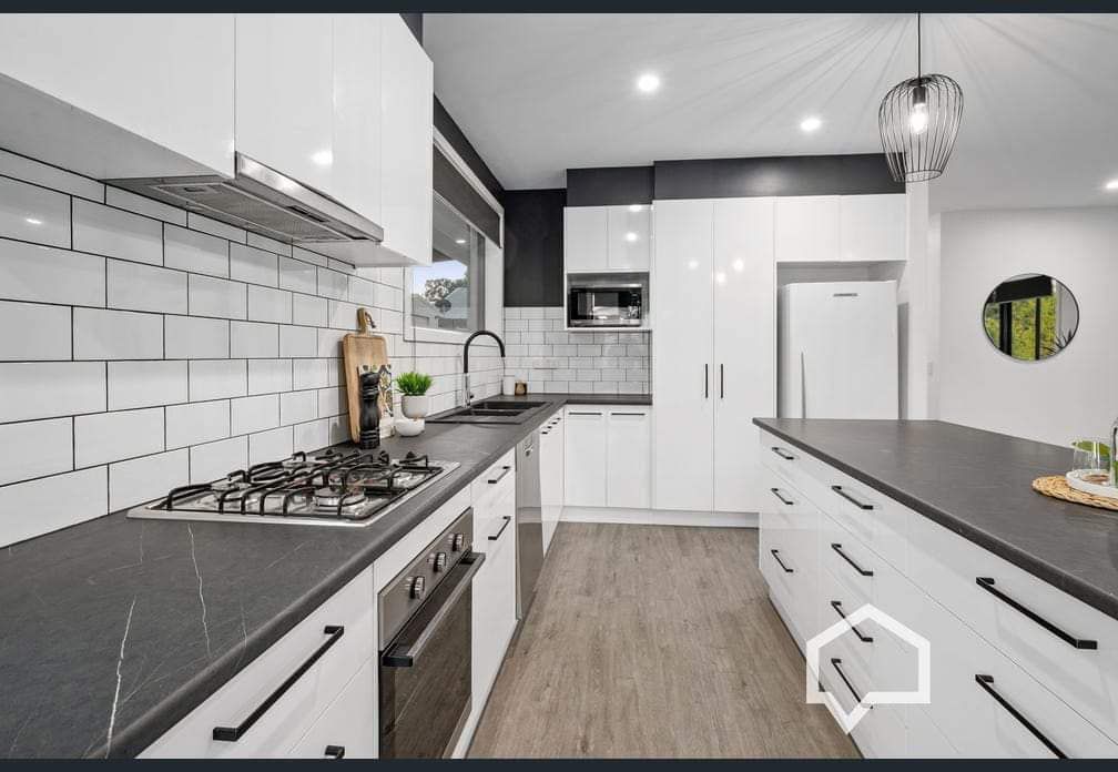 Modern kitchen with white cabinetry, dark countertops, and stainless steel appliances. Includes a kitchen island.