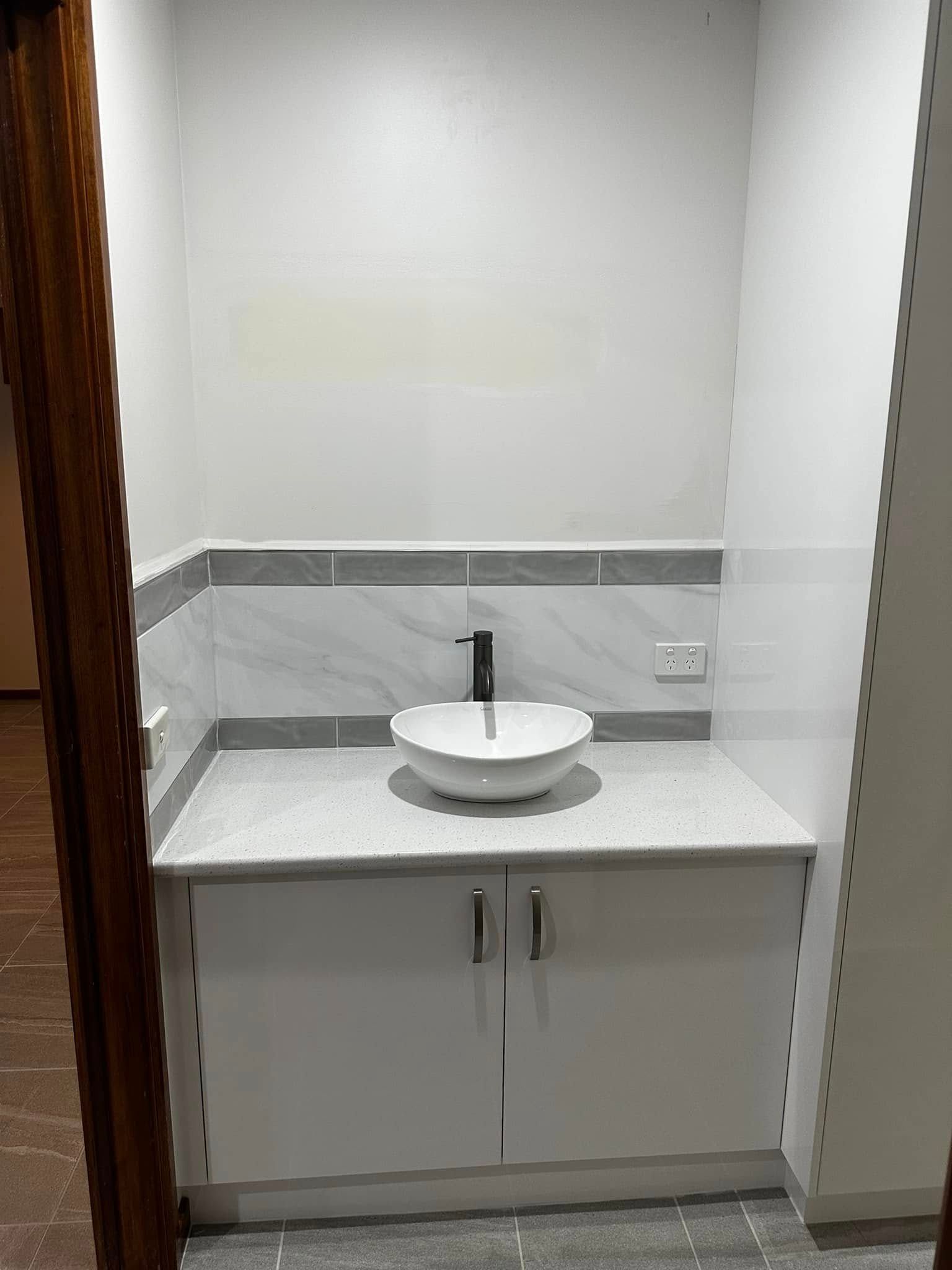 Small bathroom with a white sink bowl on a white countertop over a white cabinet. Gray tile border. White walls.