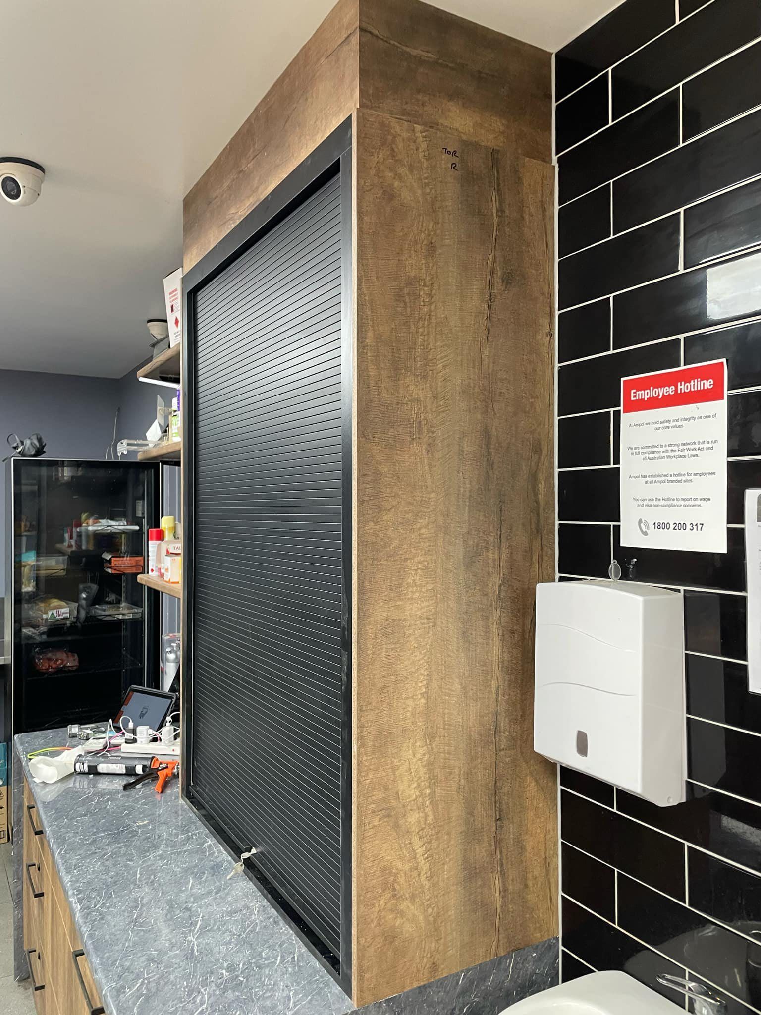 A cabinet with a patterned black sliding door next to a wall with black tile. A sign and paper towel dispenser are on the wall.