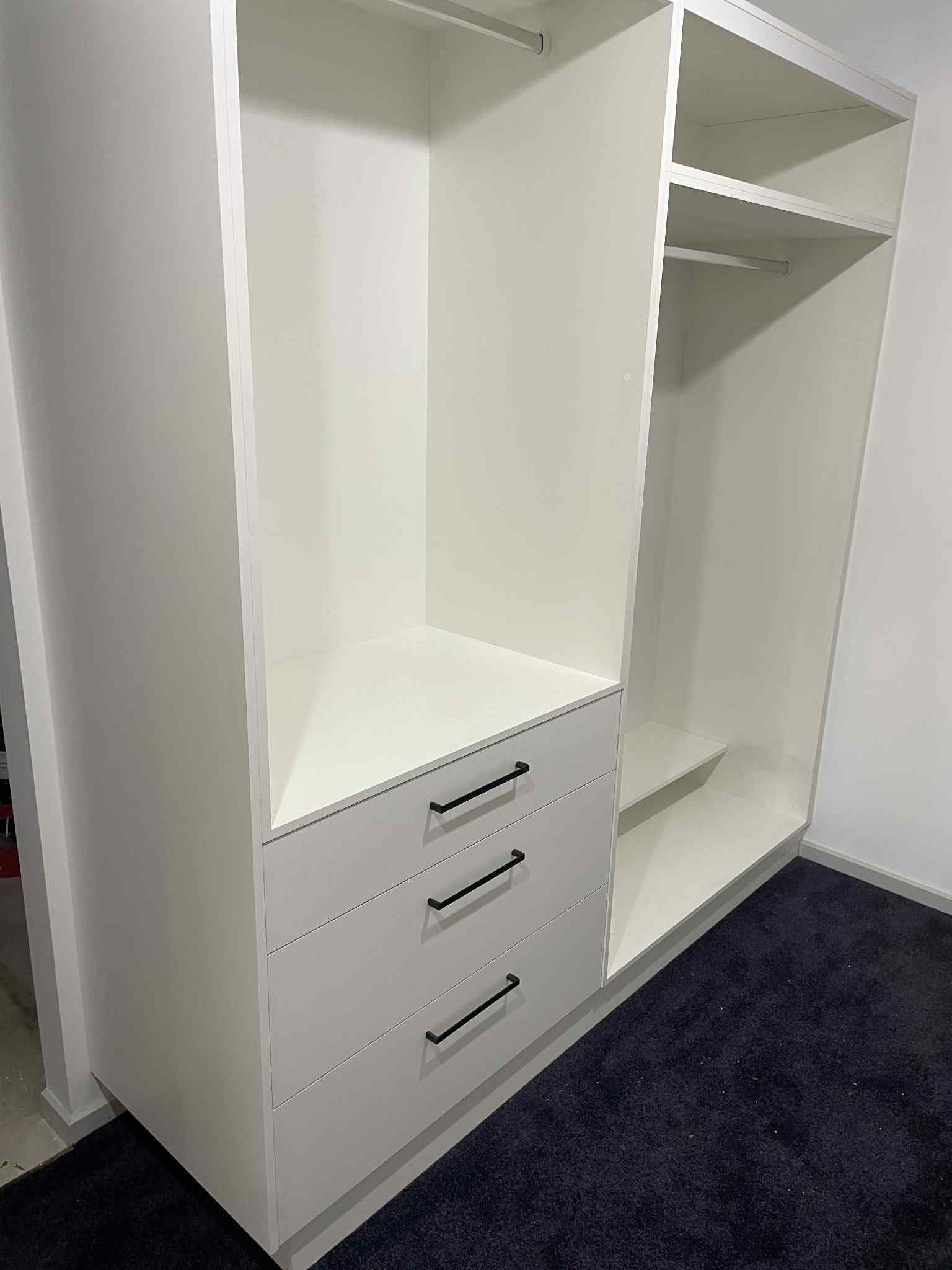 White closet with drawers and shelves. Black hardware and a dark rug in front.