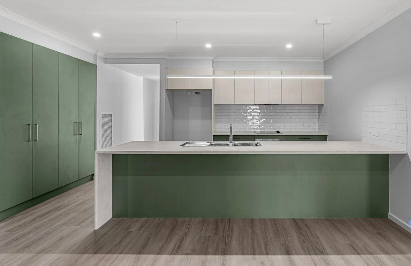 Modern kitchen with green cabinets and island, wood floors, and neutral upper cabinets, with stainless steel sink.
