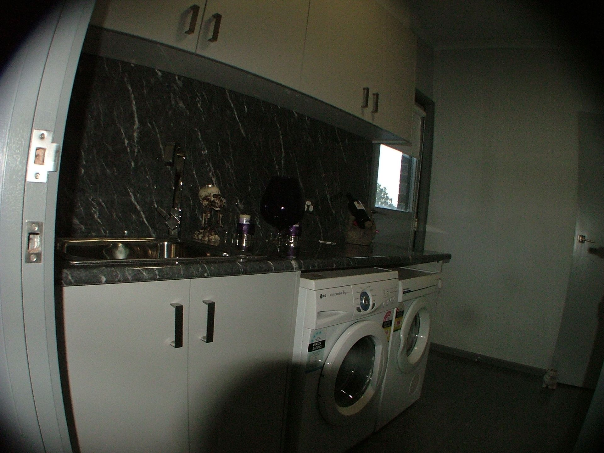 Laundry room with white cabinets, washer, and dryer. Black countertop and backsplash contrast the white appliances.