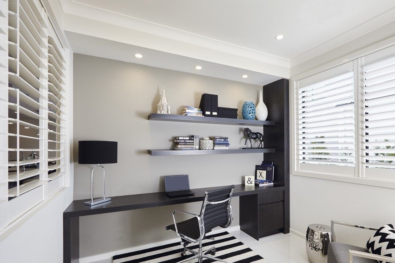 Home office with desk, shelves, and white shutters. Black and white striped rug, black desk, gray wall.