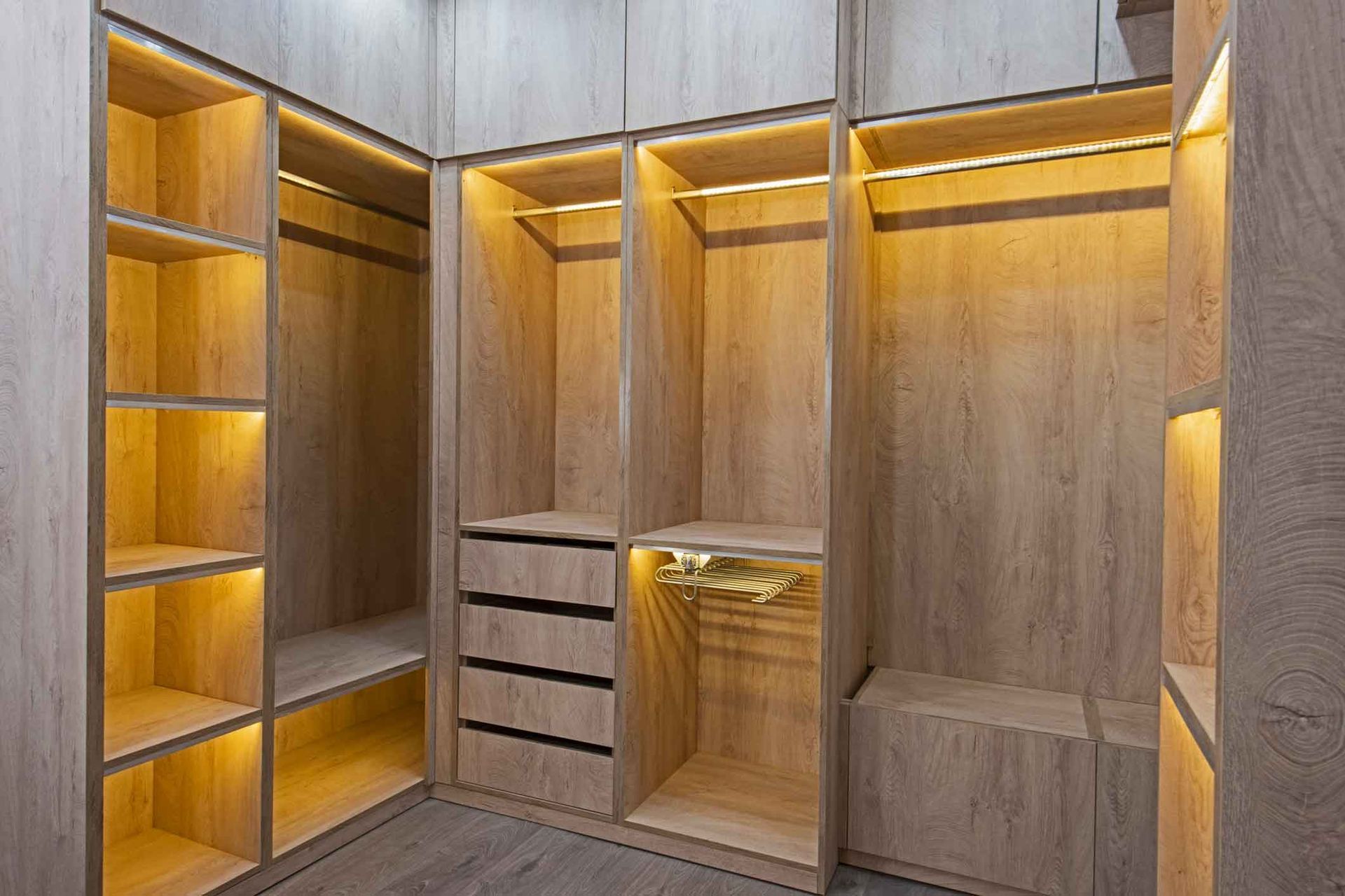 A walk-in closet with built-in wooden shelves, drawers, and hanging rods. Warm LED lighting illuminates the interior.
