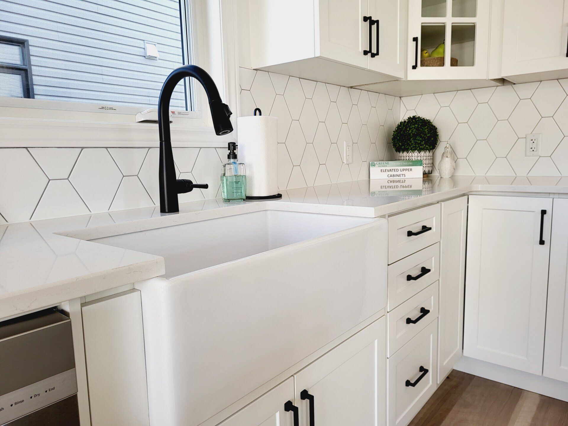 A kitchen with white cabinets and a white sink with a black faucet.