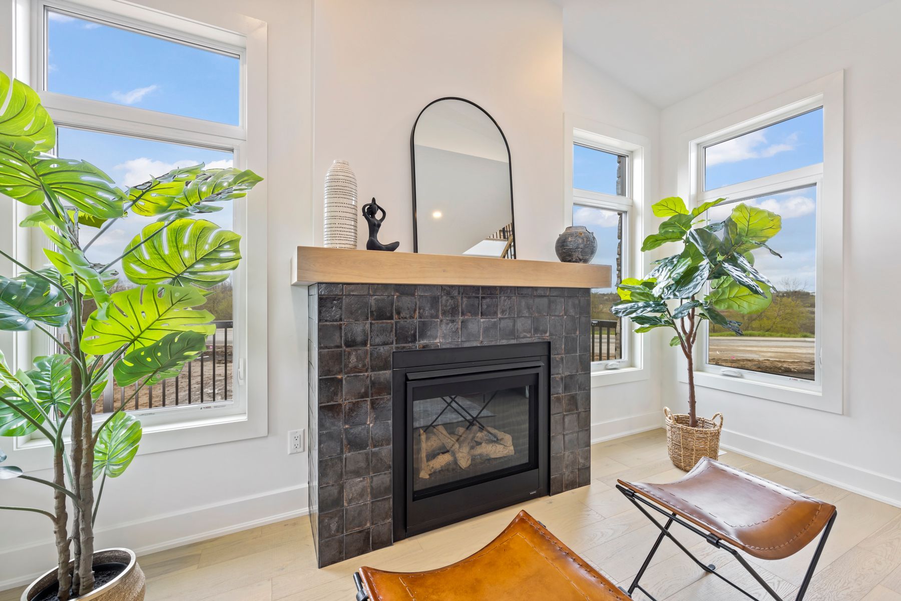 A living room with a fireplace , chairs , plants and a mirror.