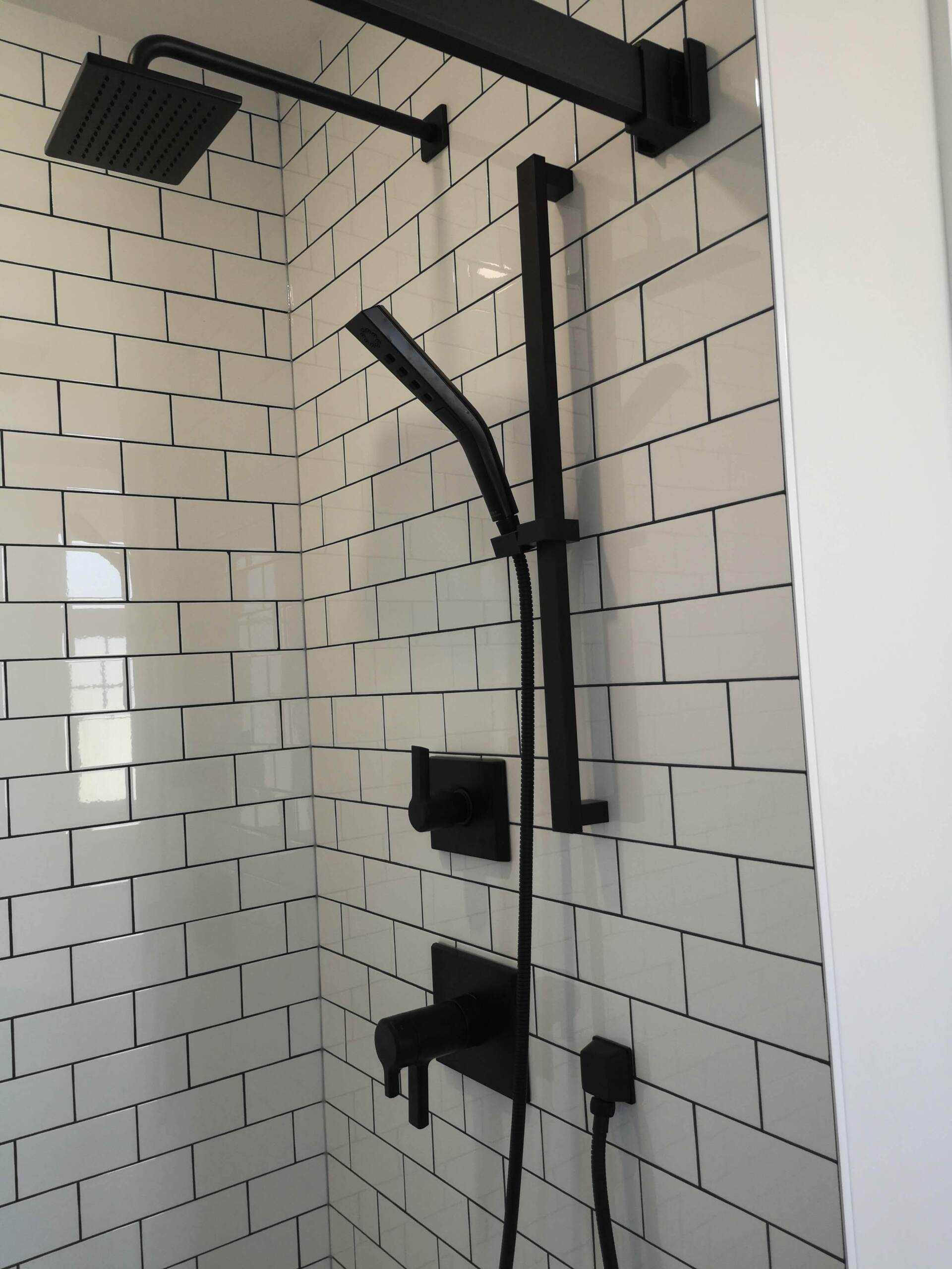 A shower with white tiles and black shower head