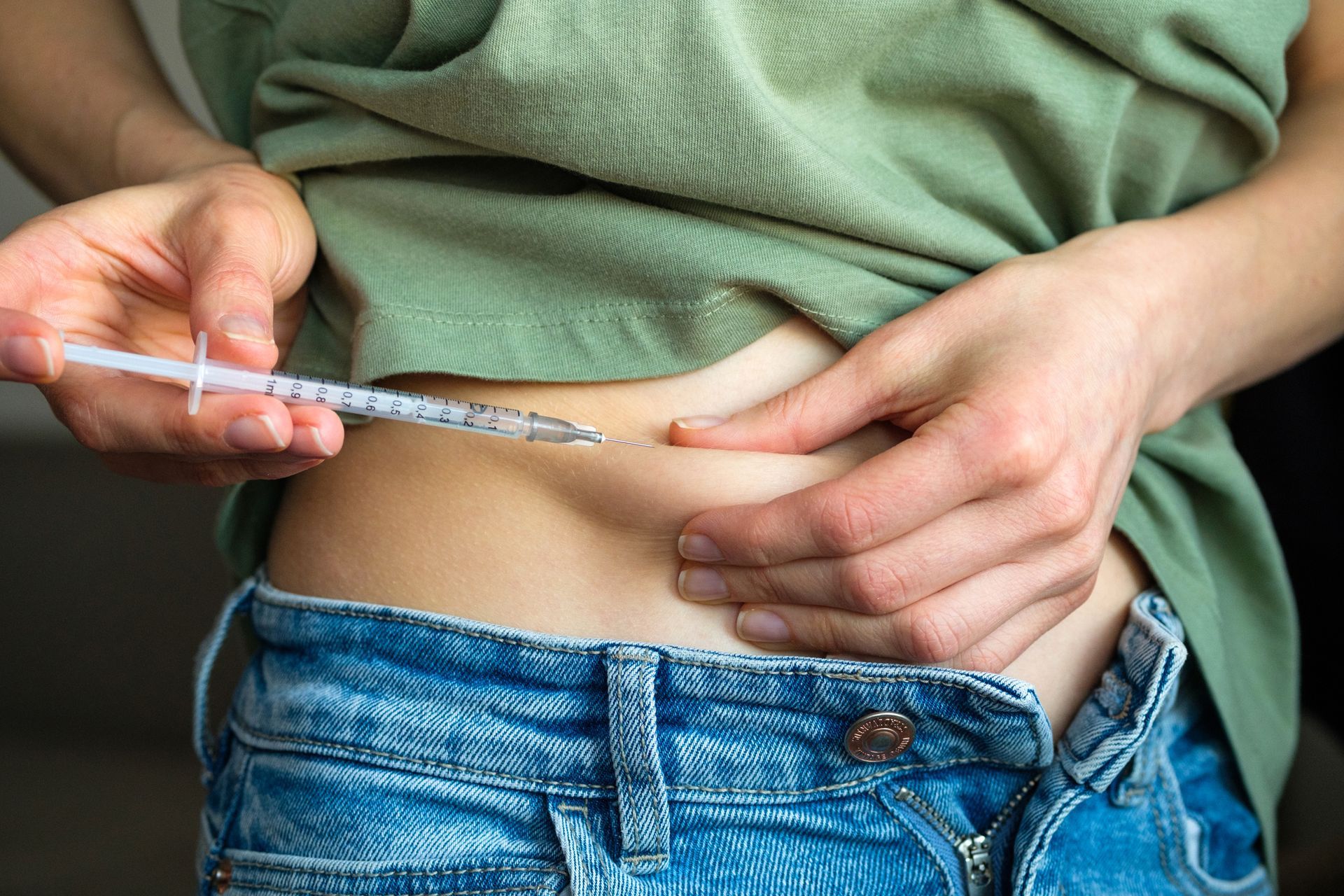A woman is getting an injection in her stomach with a syringe.